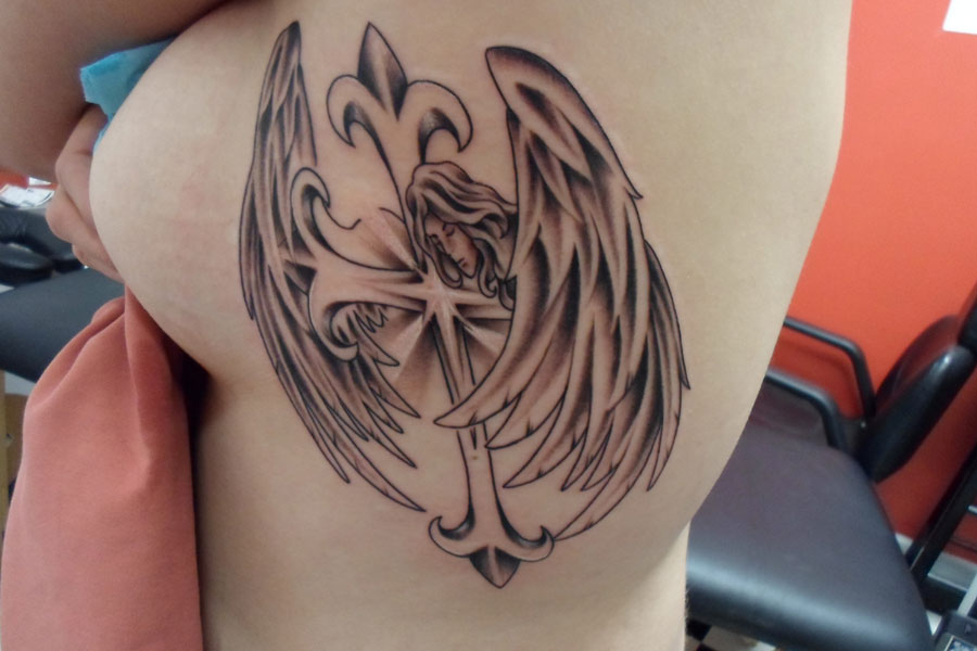 Black and grey tattoo of a winged angel resting against a fleur-de-lis cross, covering the ribs and side of the back