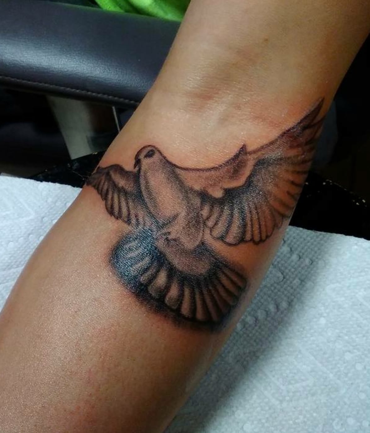 Black and grey dove in flight with wings spread and every feather picked out, wrapping the inside of the arm