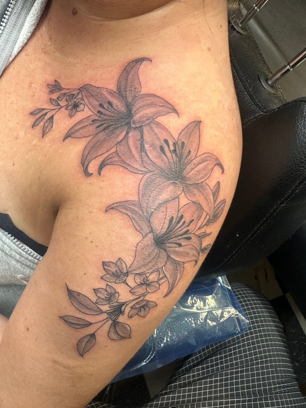 Black and grey lilies and small blossoms flowing from the shoulder down the outside of the upper arm
