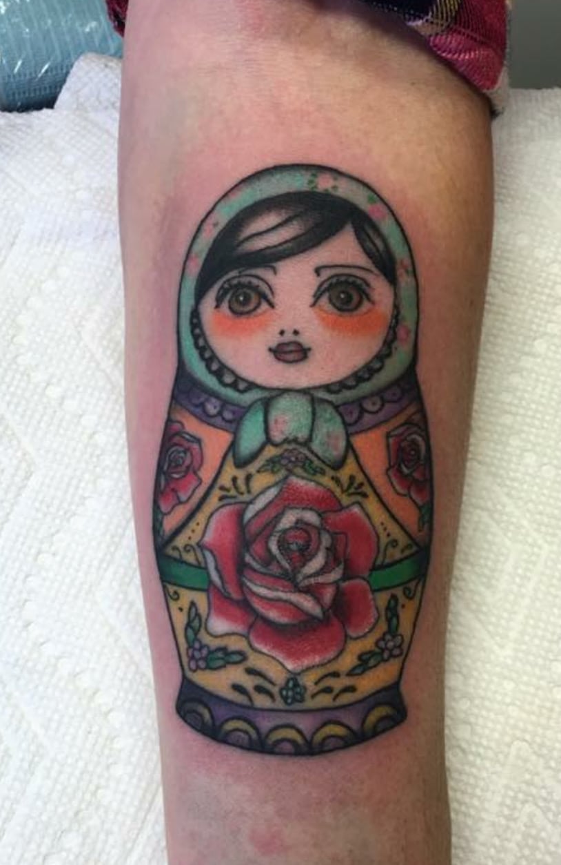Full-color tattoo of a matryoshka nesting doll painted with roses and folk patterns, on the back of an upper arm