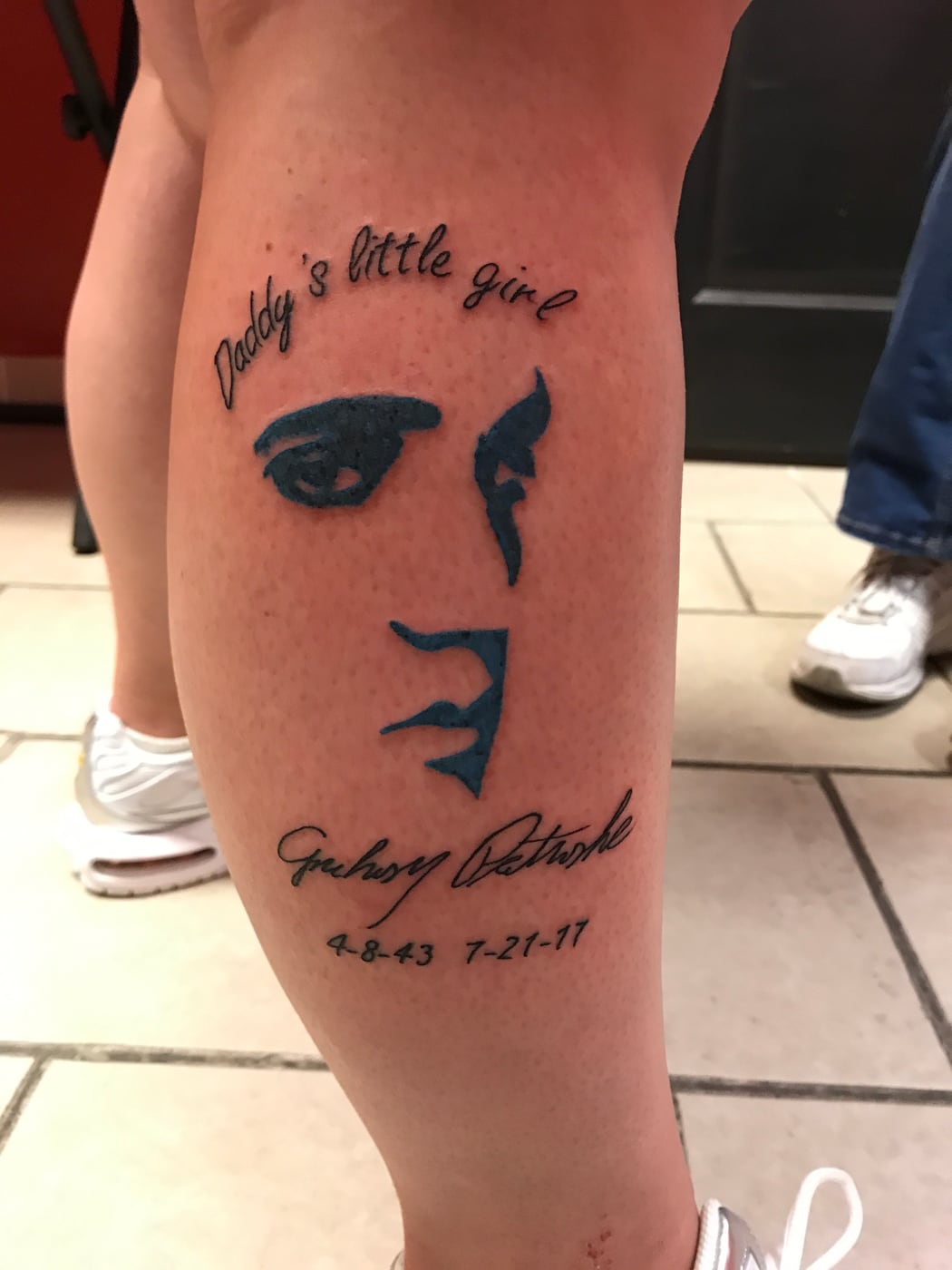Memorial calf tattoo combining a line of script, a minimal line-drawn face, a traced signature and two dates
