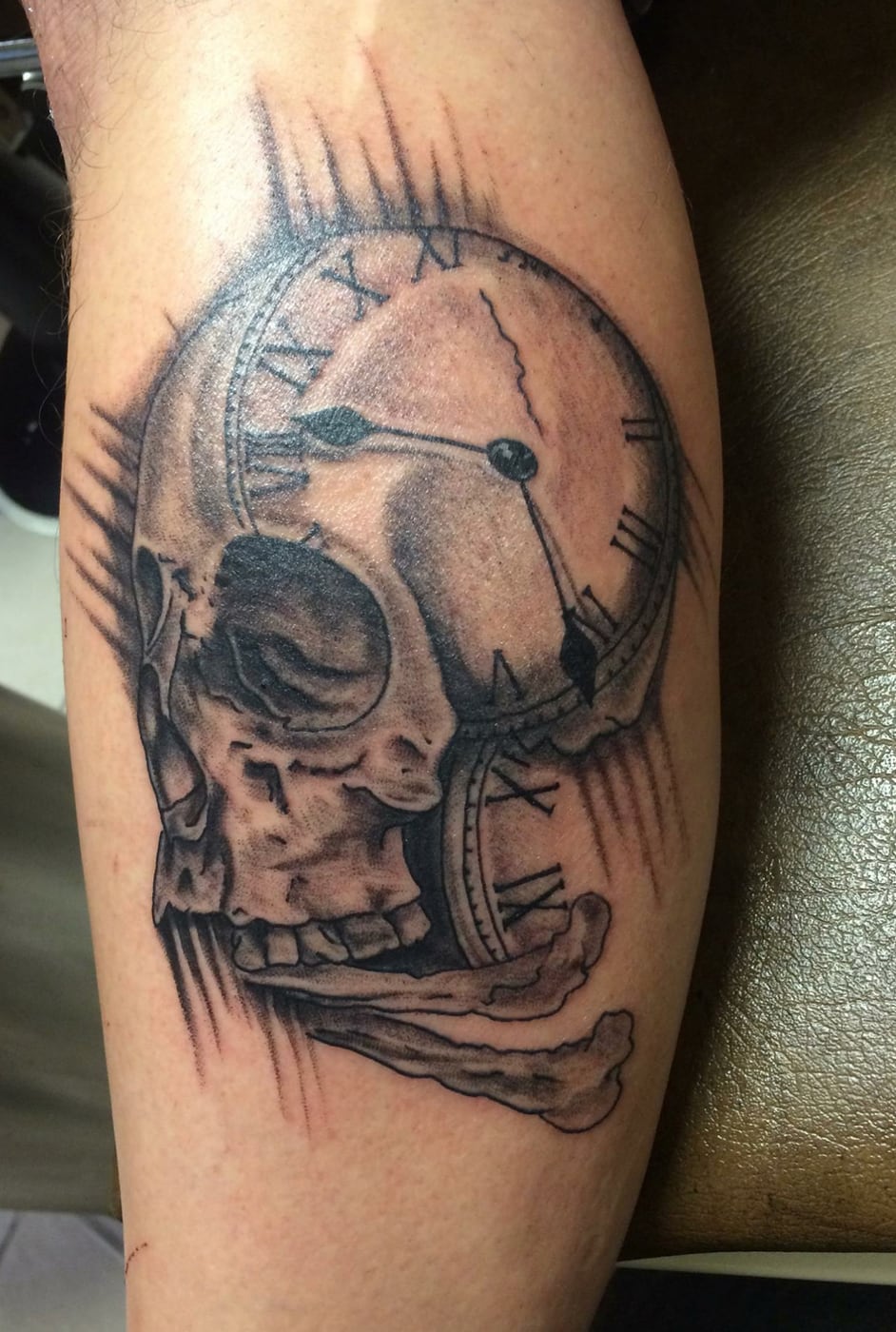 Black and grey calf tattoo of a skull fused with a cracked pocket watch face marked in Roman numerals
