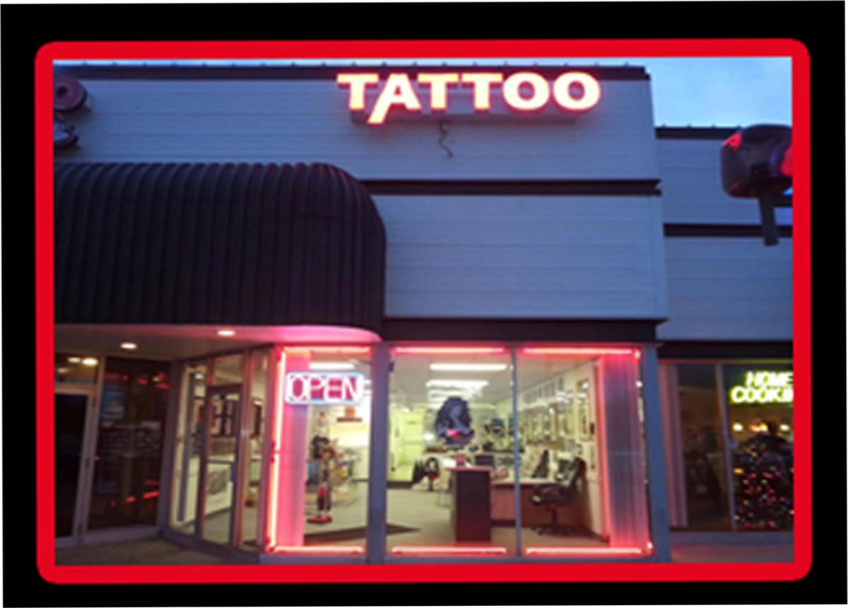Tattoo studio storefront lit at night, red neon around the windows and an illuminated TATTOO sign above the door
